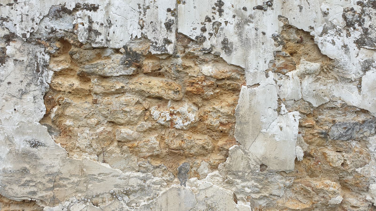 Muro in pietra antica con intonaco che si sfalda e si stacca nella fascia bassa, segno di umidità di risalita
